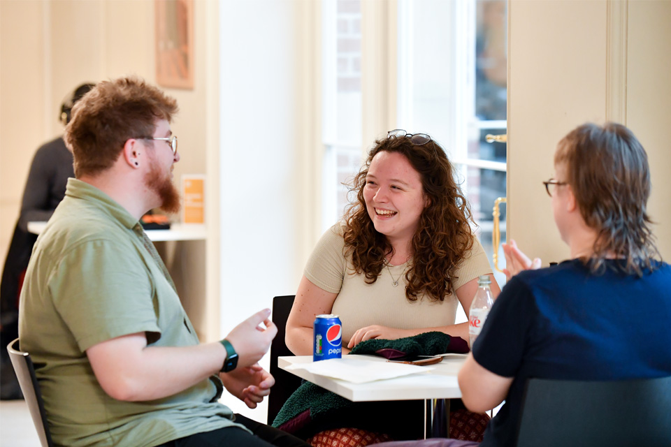 Three students talking and smiling around a table in the café.